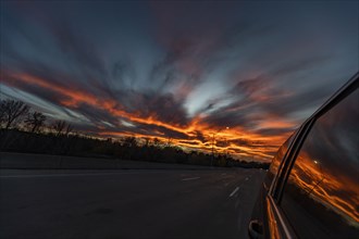 Sunset reflected in side window of car driving on freeway