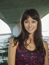 Portrait of smiling woman in sleeveless top under bridge