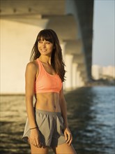 Smiling woman in sport clothing standing under bridge