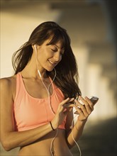 Smiling woman in sports bra holding smart phone with headphones