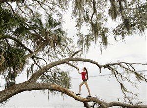 Athlete woman walking on tree branch over river