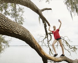 Athlete woman taking selfie on tree branch over river