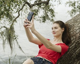 Smiling woman taking selfie on tree branch by river