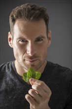 Studio portrait of man holding fresh mint leaves