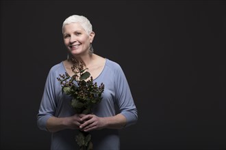 Studio portrait of smiling woman in blue shirt holding bunch of flowers