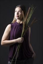 Studio portrait of woman in sleeveless purple top holding bunch of cattails