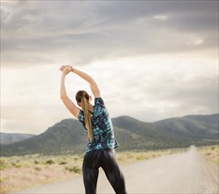 Rear view of woman stretching on road in desert landscape