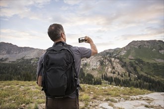 Male hiker photographing mountains with smart phone