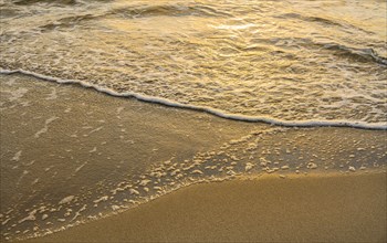 Close-up of calm ocean surf washing up onto beach at sunset