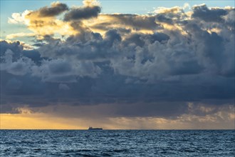 Cargo tanker ship on ocean with large clouds at sunrise