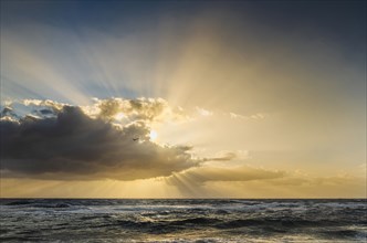Sun rays bursting from behind clouds above sea at sunrise