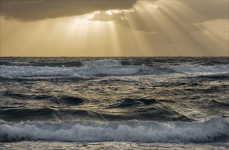 Sun rays streaking from clouds over ocean waves