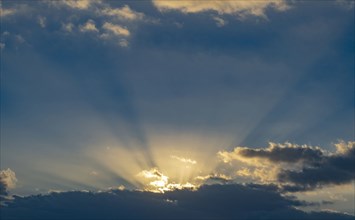 Sun rays streaking upwards from clouds against sky