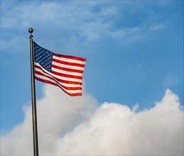 American flag on flag pole against cloudy blue sky