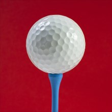 Golf ball on tee against red background