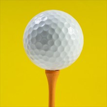 Golf ball on tee against yellow background