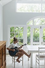 Teenage girl (16-17) playing guitar in white room
