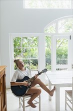 Teenage girl (16-17) playing guitar in white room