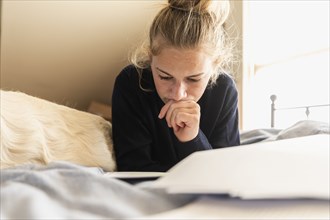Teenage girl (16-17) lying on bed with dog and reading