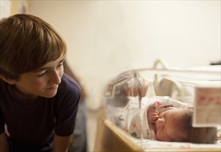 Boy (12-13) looking at newborn baby sister (0-1 months) in incubator