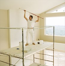 Painter on scaffolding using roller to paint ceiling