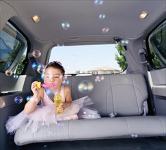 Girl (6-7) in ballet outfit blowing bubbles in car