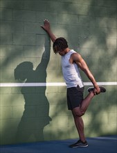 Athletic man stretching leg at wall