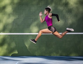 Athletic woman with prosthetic arm running against wall