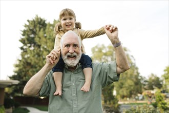 Portrait of smiling senior man carrying on shoulders granddaughter