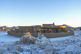 Pueblo style house in snow covered landscape at sunset