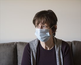 Anxious woman in face mask sitting on sofa