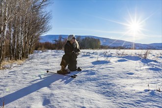 Senior blonde woman with snow shoes looking at snow covered landscape on sunny day