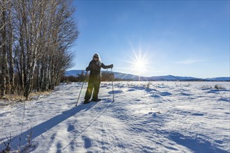 Senior blonde woman snow shoeing in snow covered landscape on sunny day