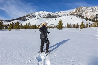 Senior blonde woman snow shoeing in snow covered landscape