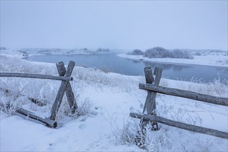 Wooden fence in snow covered field near river