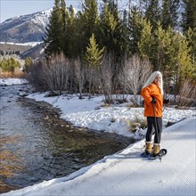 Senior blonde woman snowshoeing in snow covered landscape