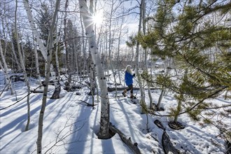 Senior blonde woman snowshoeing in snow covered forest