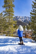 Rear view of senior blonde woman with snowshoes in snow covered landscape