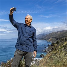 Smiling senior man taking selfie at Big Sur coast