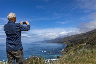 Rear view of senior man photographing Big Sur coast