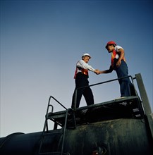 Two workers shaking hands on industrial platform