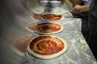 Man putting tomato sauce onto fresh hand made pizzas