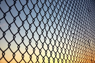 Chain link fence against sky at sunset