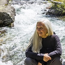 Senior blonde woman resting by rushing stream near Sun Valley
