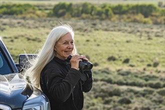 Smiling woman with binoculars at car in field