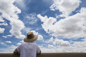 Rear view of woman looking over wall at cloud sky