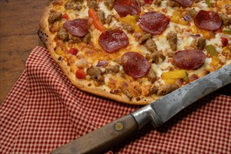 Pizza on wooden table with antique knife and red check cloth