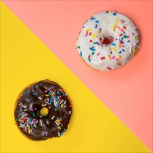 Overhead view of two donuts with icing and sprinkles on multi-Ced background