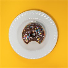 Overhead view of eaten donut with chocolate icing and sprinkles on white plate