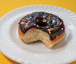 Eaten donut with chocolate icing and sprinkles on white plate